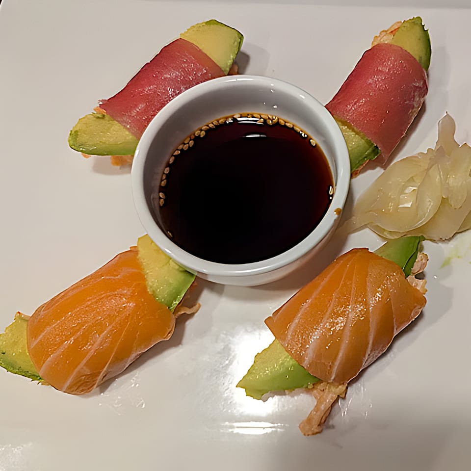 Four sushi pieces, two with tuna and two with salmon, wrapped around avocado, with soy sauce and ginger.