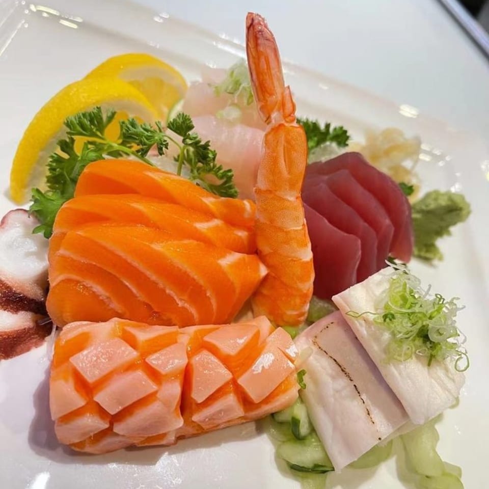 A colorful sashimi platter with salmon, tuna, shrimp, and octopus, garnished with lemon and parsley.