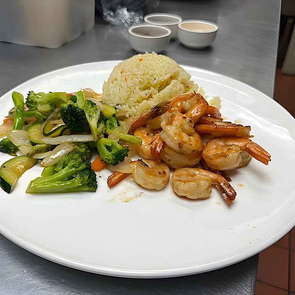 Hibachi shrimp and scallops with fried rice and mixed vegetables on a white plate.
